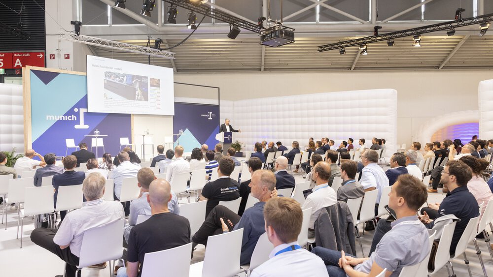 Interessierte Besucher lauschen einem Vortrag zum Thema „Robot foundation models“ auf der „munich i“ Bühne.