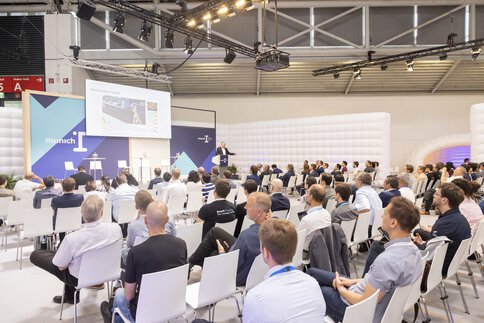 Interessierte Besucher lauschen einem Vortrag zum Thema „Robot foundation models“ auf der „munich i“ Bühne.