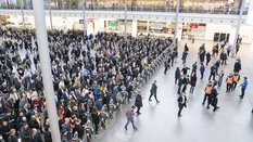 Blick von der Seite über die Eingangshalle der productronica Messe mit zahlreichen wartenden Besuchern an der Ticketkontrolle. Einige Besucher sind schon hindurch.