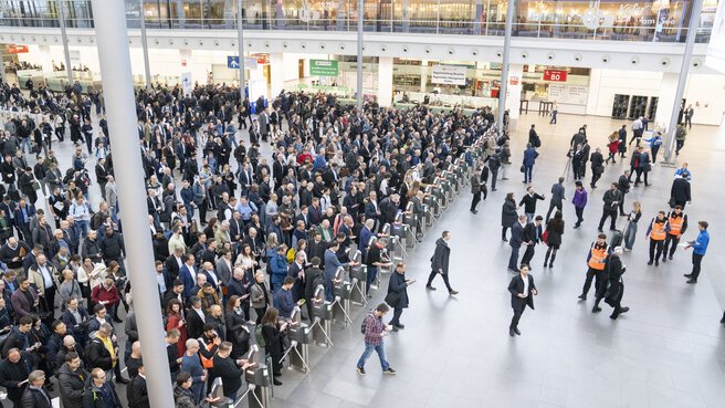 Blick von der Seite über die Eingangshalle der productronica. Eine große Menschenmenge hat sich vor der Ticketkontrolle versammelt und passiert diese gerade.