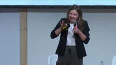 Eine Frau im schwarzen Blazer spricht mit einem Mikrofon auf der bauma.