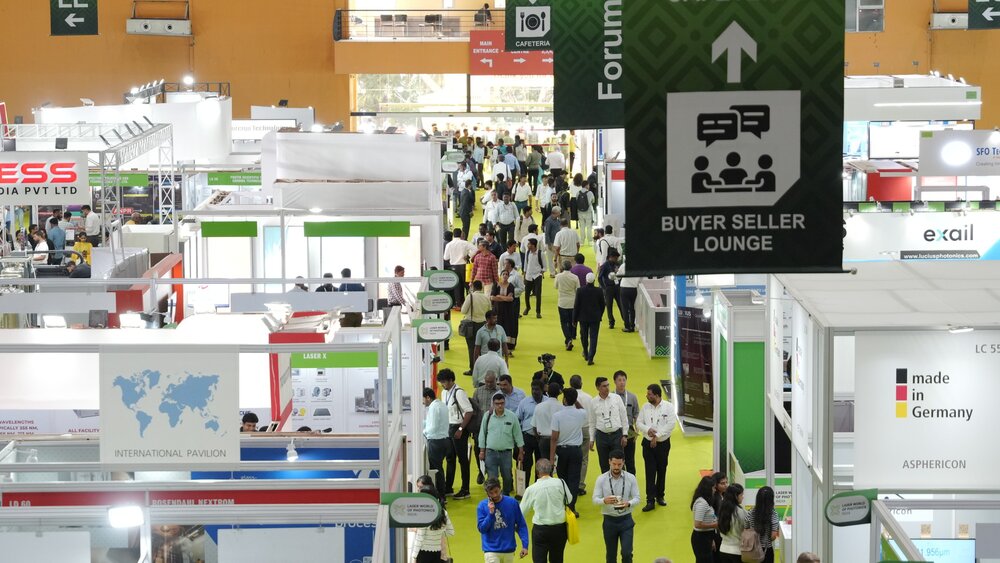 View across a well-attended hall at Laser World of Photonics India with numerous exhibition stands and banners hanging from the ceiling.