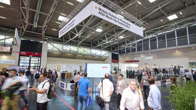 People walk through an exhibition hall with stands and a cordoned-off demonstration area.