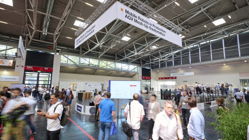 People walk through an exhibition hall with stands and a cordoned-off demonstration area.