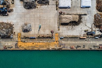  Luftaufnahme eines Schrottplatzes am HafenLuftaufnahme eines Industrie- und Verladebereichs am Wasser mit Schrott- und Materialhaufen sowie mehreren Baumaschinen.