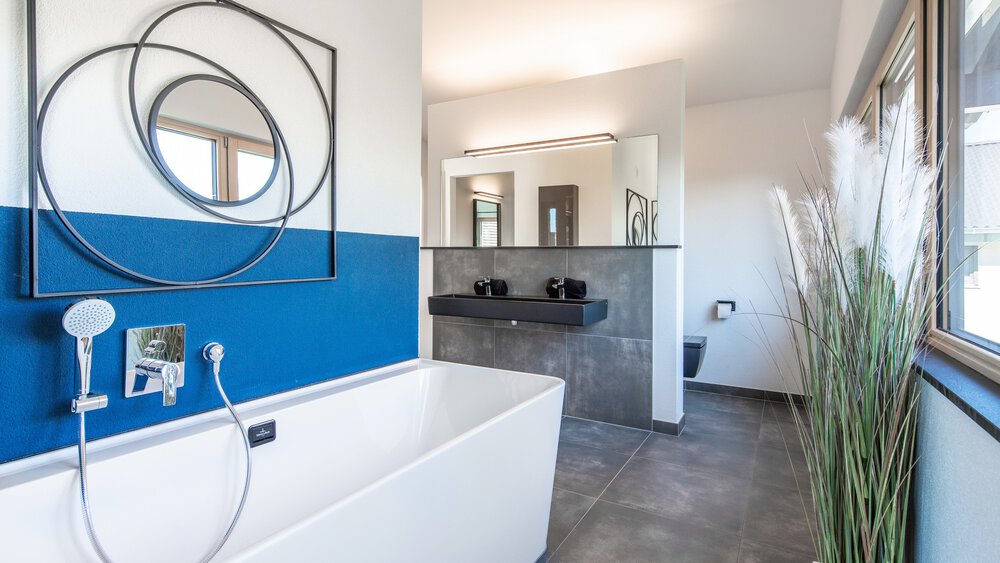 Modernes Badezimmer mit weißer Badewanne, abstrakter Wandkunst, großem Spiegel und elegantem Waschtisch.