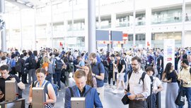 A large group of people stand in front of the ticket barriers in the exhibition entrance hall.