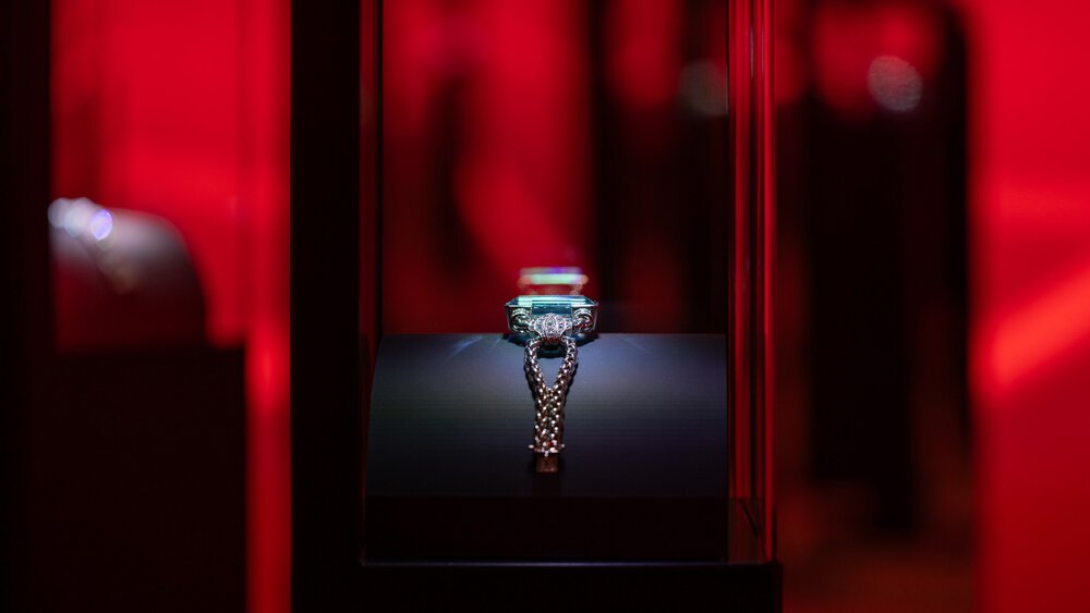 A silver trophy in a glass display case, illuminated against a dark red background.
