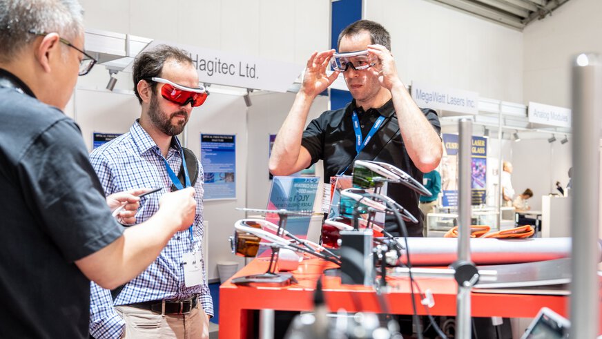 Two people try on modern safety goggles at an exhibition stand.