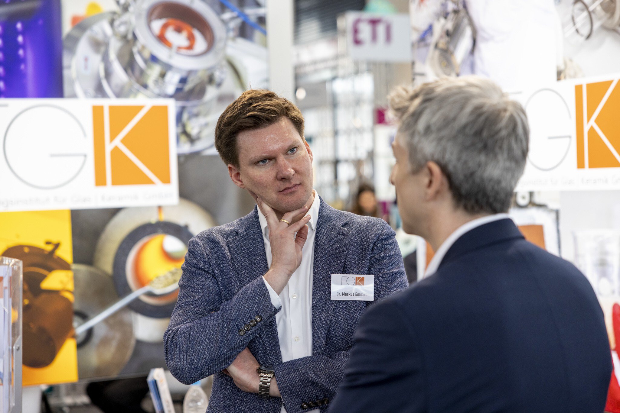 Two men in conversation at an exhibition stand surrounded by posters and display walls.