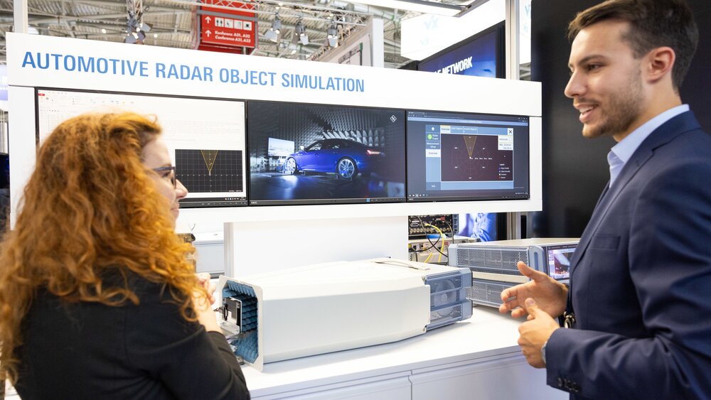 A woman and a man are talking at an exhibition stand with displays on the subject of 