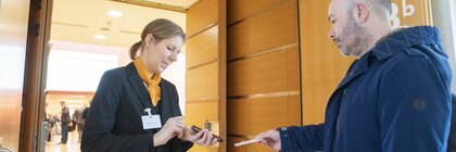 A woman in a suit scans a presented ticket with a smartphone.