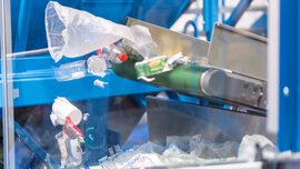 Plastic waste such as films, cups, and bottles on a conveyor belt in a sorting facility.