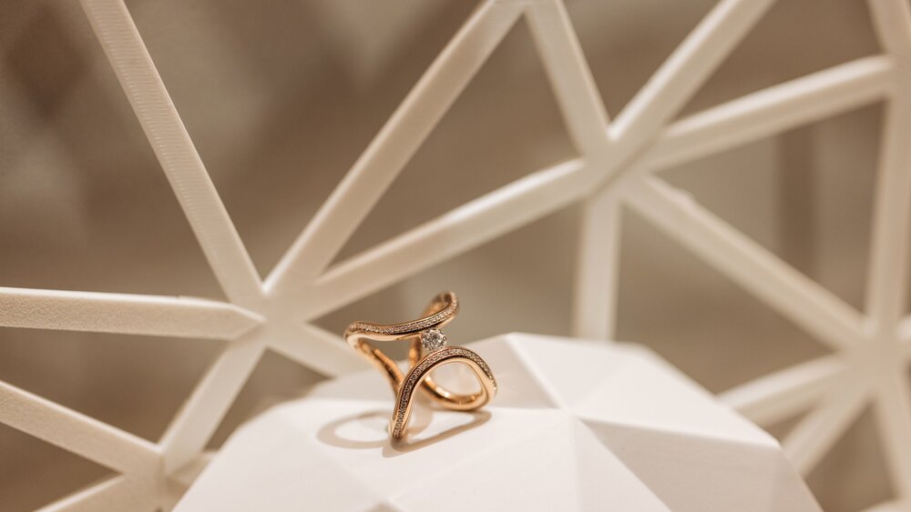 A close-up view of an intertwined double ring set with a gemstone, displayed on an abstract surface for presentation purposes.