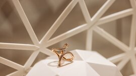A close-up view of an intertwined double ring set with a gemstone, displayed on an abstract surface for presentation purposes.