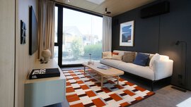 Modernes Wohnzimmer mit weißem Sofa, buntem Teppich, Couchtisch und großem Fenster mit Blick nach draußen.