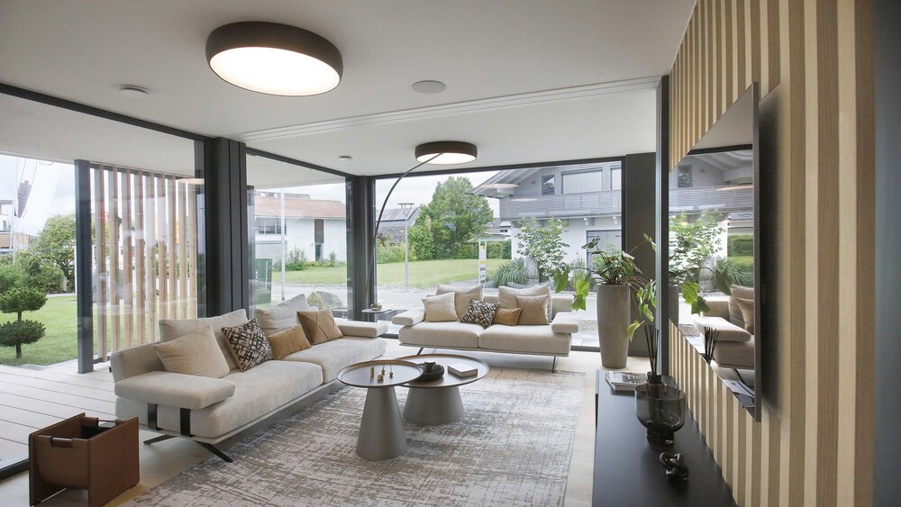 Modernes Wohnzimmer mit großen Fenstern, zwei beigen Sofas, rundem Couchtisch und Blick auf den Garten.