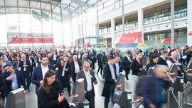 Eine Eingangshalle zur ceramitec mit zahlreichen Messebesuchern, die sich auf die Ticketkontrollen zubewegen. Im Hintergrund erkennt man einen Ticketverkaufsschalter.