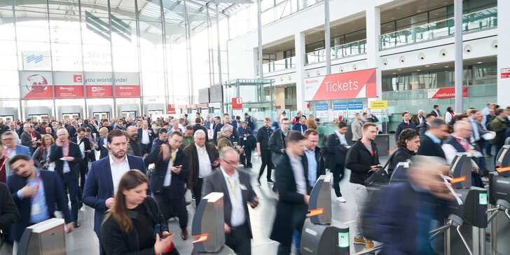 The entrance hall to ceramitec, filled with numerous trade fair visitors making their way towards the ticket checks. A ticket sales counter can be seen in the background.
