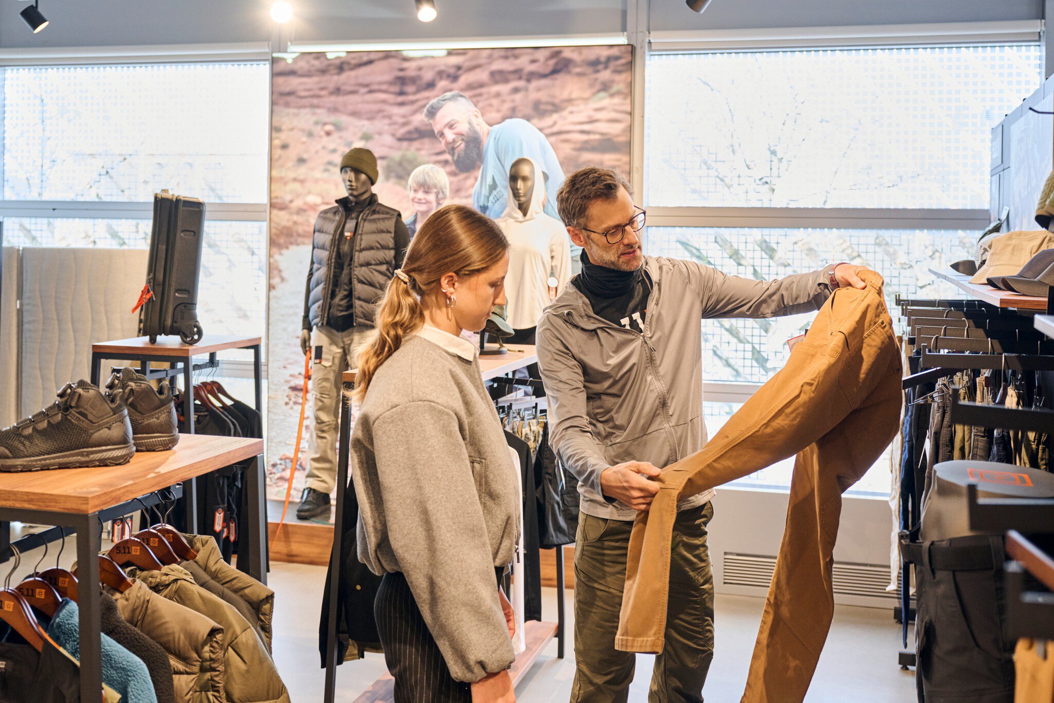 Ein Mann und eine Frau stehen in einem Ausstellungsbereich für Outdoor-Bekleidung und -Schuhe und betrachten eine beige Hose.