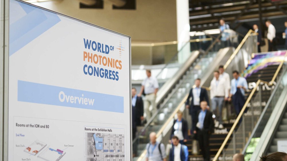 Sign with an overview map of the World of Photonics Congress. An escalator with people can be seen blurred in the background.