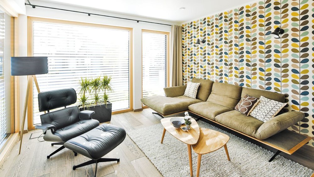 Wohnzimmer mit gemusterter Akzentwand, grünem Sofa, schwarzem Loungesessel, Couchtisch und Stehlampe.