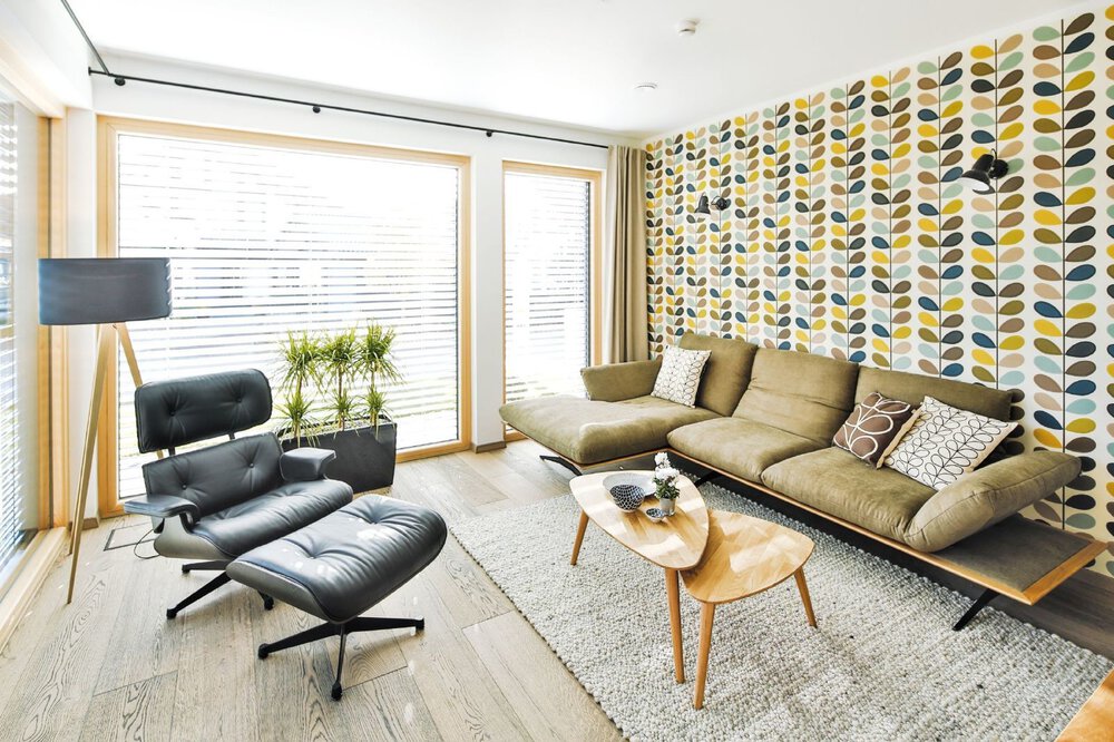 Wohnzimmer mit gemusterter Akzentwand, grünem Sofa, schwarzem Loungesessel, Couchtisch und Stehlampe.