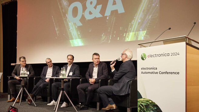Five men in suits sit on the electronica stage for a question-and-answer session.