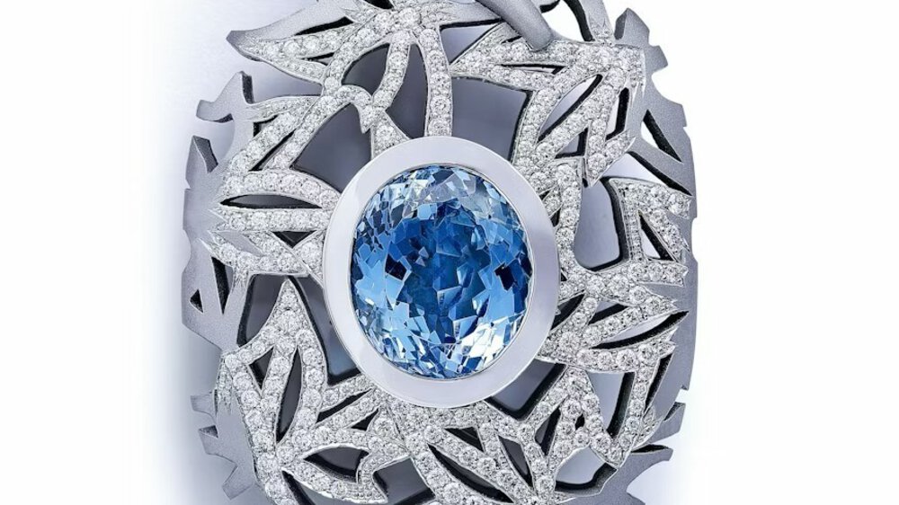 A close-up view of a delicate silver piece of jewelry with numerous tiny diamonds and a large blue oval diamond in the center.