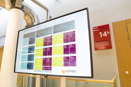 A large screen with a color-coded schedule and the words Overview Conference Program.