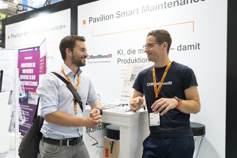 Two men are talking at the booth at automatica; the focus is on networking and discussing the future of smart automation and robotics.