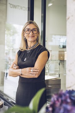 Eine lächelnde Frau mit schulterlangen blonden Haaren, einer großen Brille und mehreren Halsketten, Ohrringen, Armbändern und Ringen.