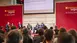 The panelists discuss on the stage of a transportation logistics exhibition while the audience sits and screens are behind them.
