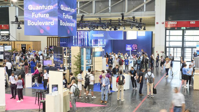 Reges Treiben auf dem Quantum Future Boulevard der World of Quantum in München mit zahlreichen Besucher:innen und Ausstellerständen.