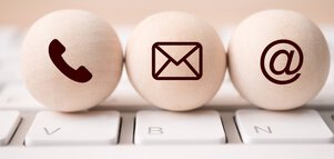 Three wooden balls on a white keyboard, printed with the symbols telephone receiver, envelope and @ sign.