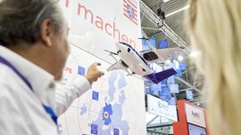 A man points at a blue and white drone shaped like a miniature airplane.