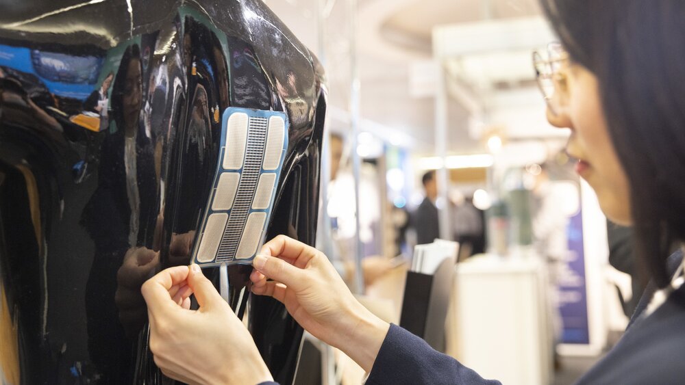 Eine Frau bringt auf der LOPEC Messe einen Aufkleber mit elektronischen Schaltkreisen auf dem Rücken einer glänzend schwarzen Schaufensterpuppe an.