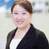 Smiling woman with brown, tied-up hair in a black blazer with a white blouse.