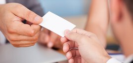 Two people exchange a small white business card in a professional setting.