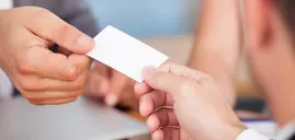 Two people exchange a small white business card in a professional setting.