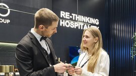 Two people exchange business cards at an exhibition booth while engaging in a conversation in a modern hospitality setting.