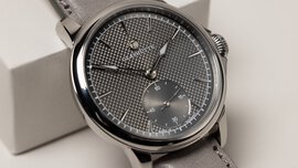 Close-up view of a wristwatch with a finely grained silver dial with a separate dial for the second hand and a gray wristband.