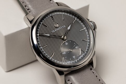 Nahansicht einer Armbanduhr mit einem fein gemaserten silbernen Ziffernblatt mit einem separaten Ziffernblatt für den Sekundenzeiger und einem grauen Armband.