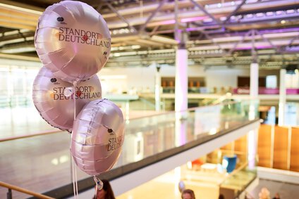 auf dem Bild sieht man einen Ballon uaf den hingezoomt wird in einem grßen beleudhteten Saal, auf dem Ballon steht Standort Deutschland