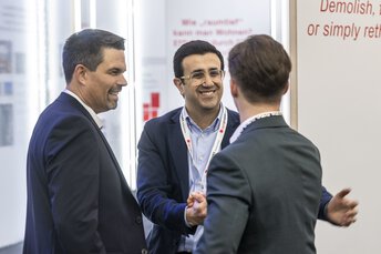 Three men in business attire greeting each other with a handshake at EXPO REAL