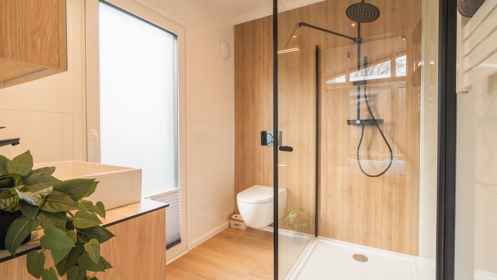 Ein modernes holzvertäfeltes Bad mit einer bodentiefen Tür mit Milchglas, durchsichtiger Duschkabine, WC und Waschbecken.