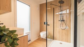 Ein modernes holzvertäfeltes Bad mit einer bodentiefen Tür mit Milchglas, durchsichtiger Duschkabine, WC und Waschbecken.