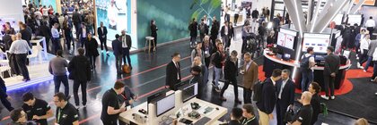 Menschenmassen versammeln sich auf einer belebten Technologiemesse mit Ständen, Displays und Menschen, die in einer großen Ausstellungshalle interagieren.