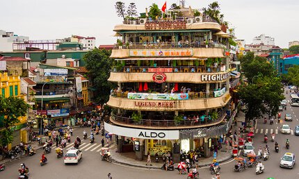 Multi-storey building with stores and cafés on a busy street corner full of motorcycles and people.