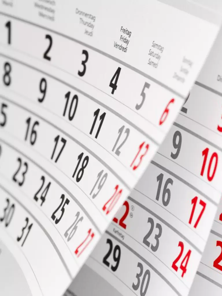 Curved pages of a calendar showing a month with numbers in black and Sundays in red.